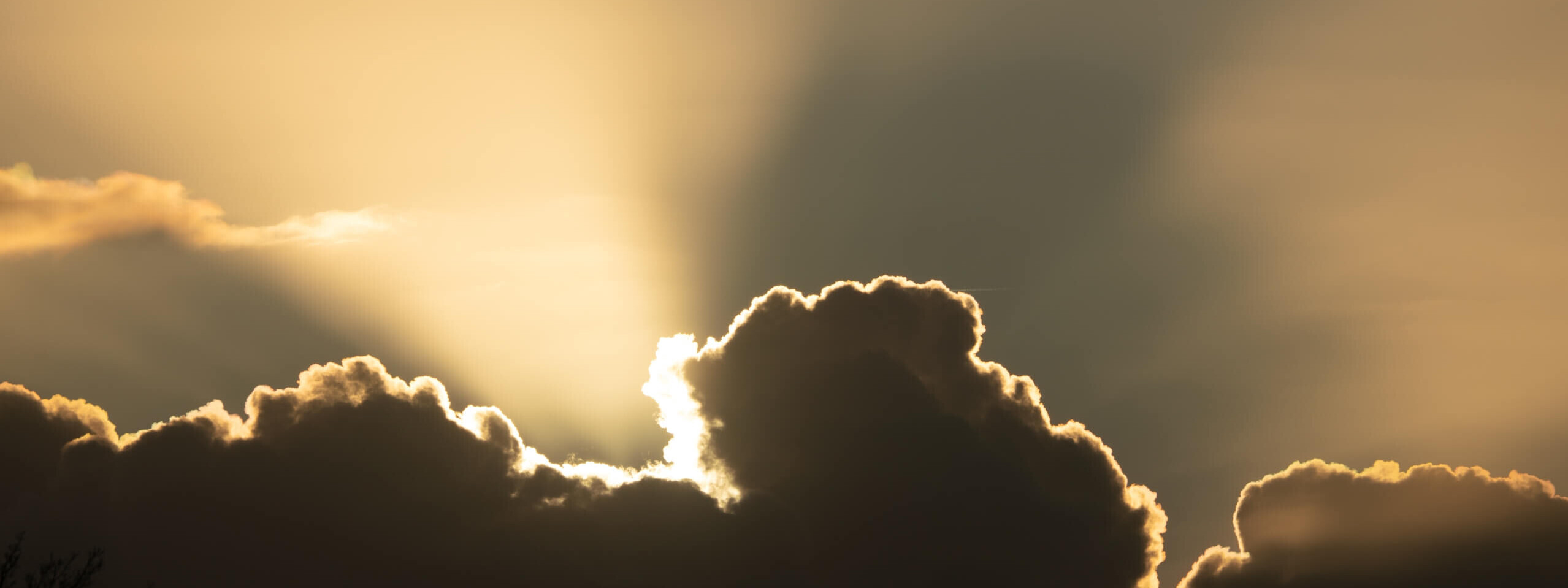 Die Silhouette von Wolken wird von goldenem Licht durchzogen, während die Sonne hinter ihnen verschwindet.