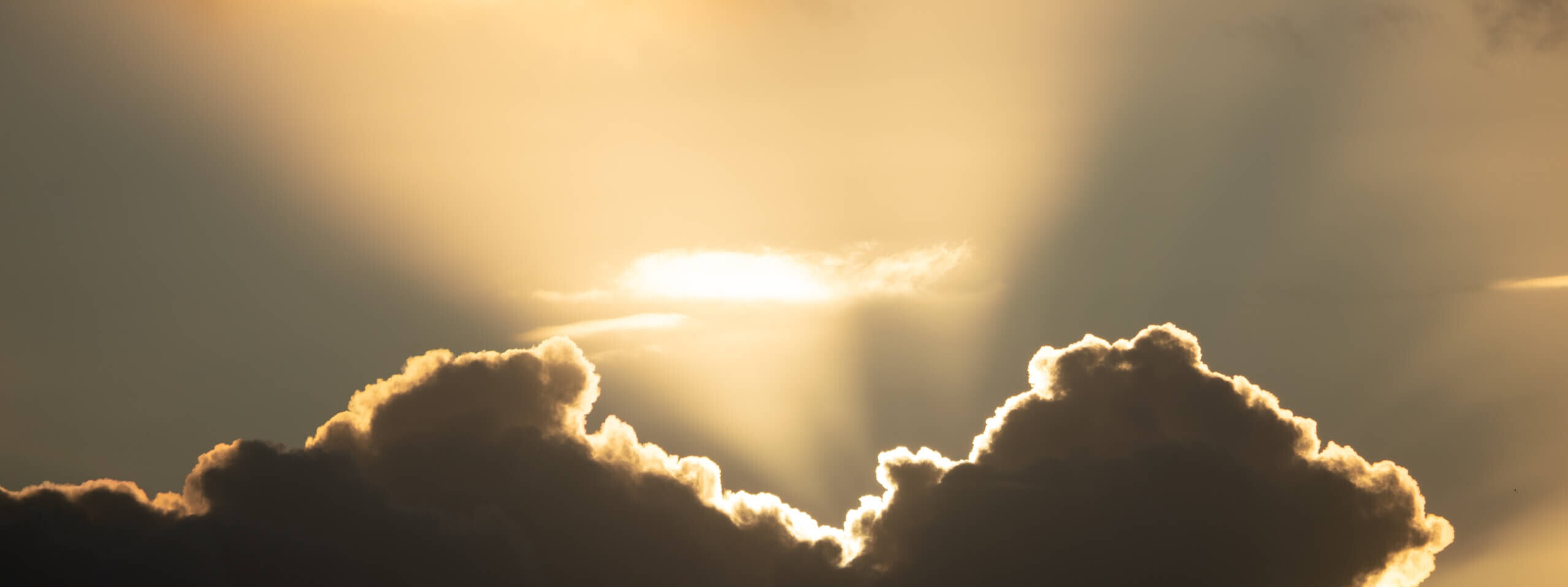 Die Sonne strahlt durch die Wolken und erzeugt einen dramatischen Lichtstrahl, der den Himmel erhellt.